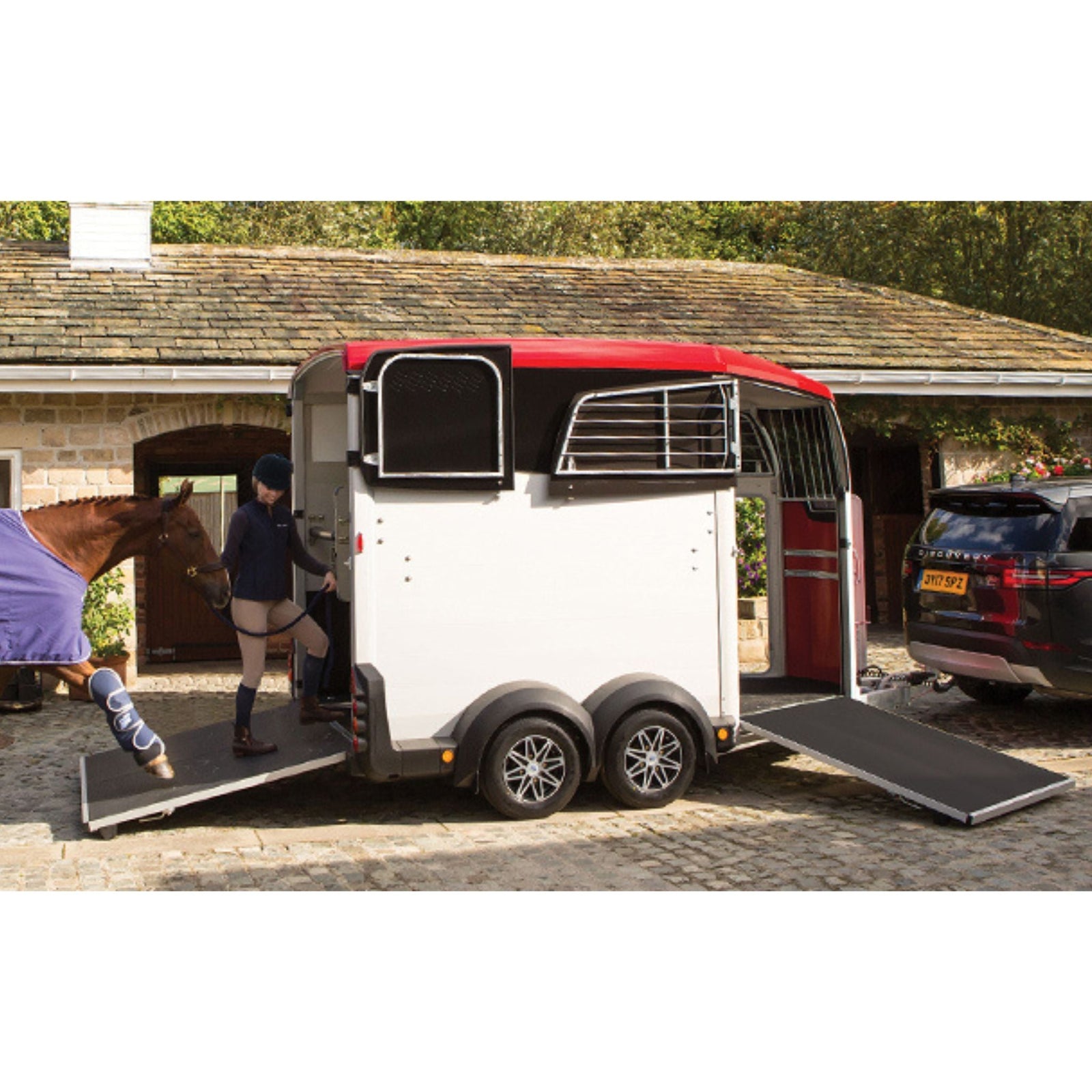 Two horses standing in red horse float, with ramp down.