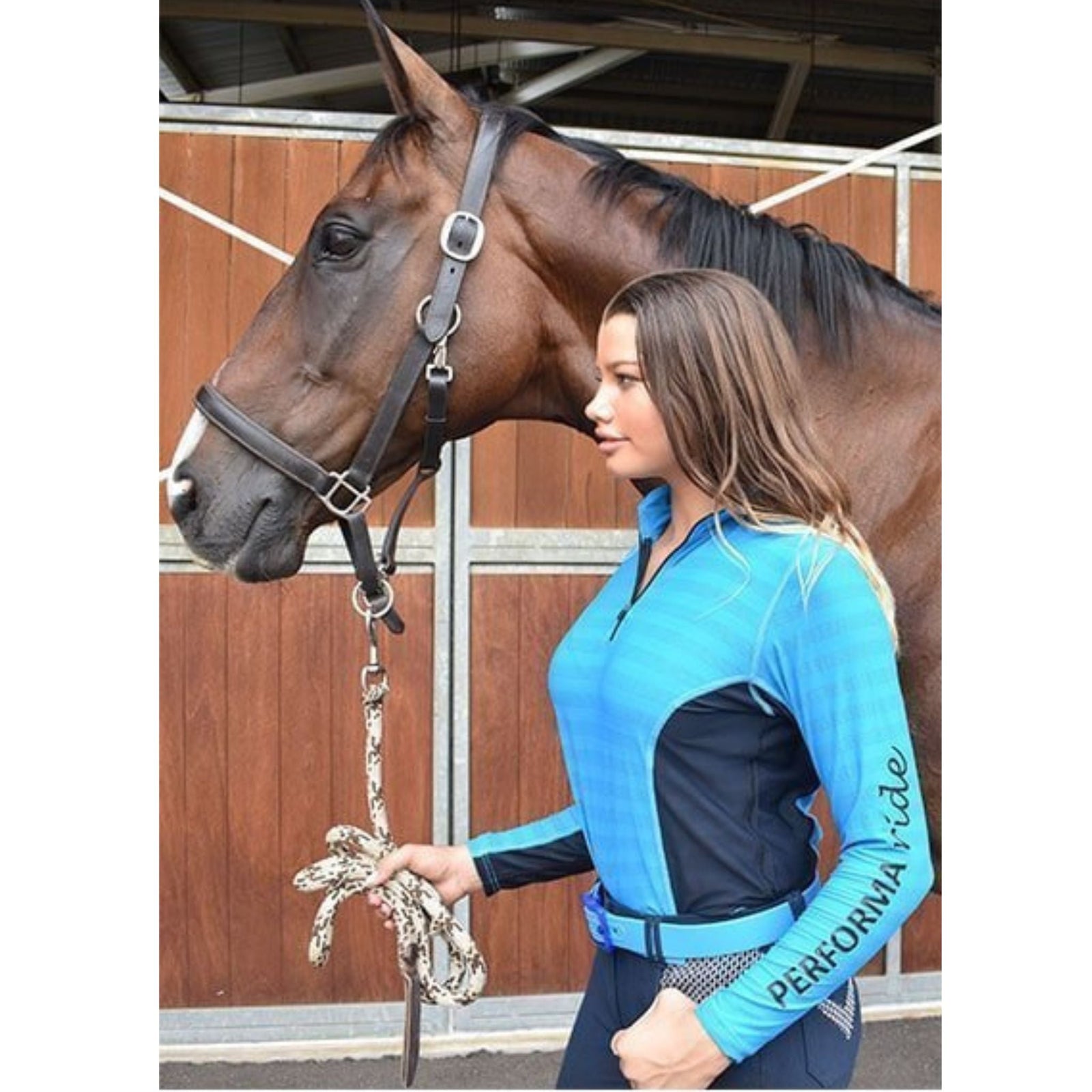 Lady wearing aqua long sleeve riding shirt with navy sides, holding horse.