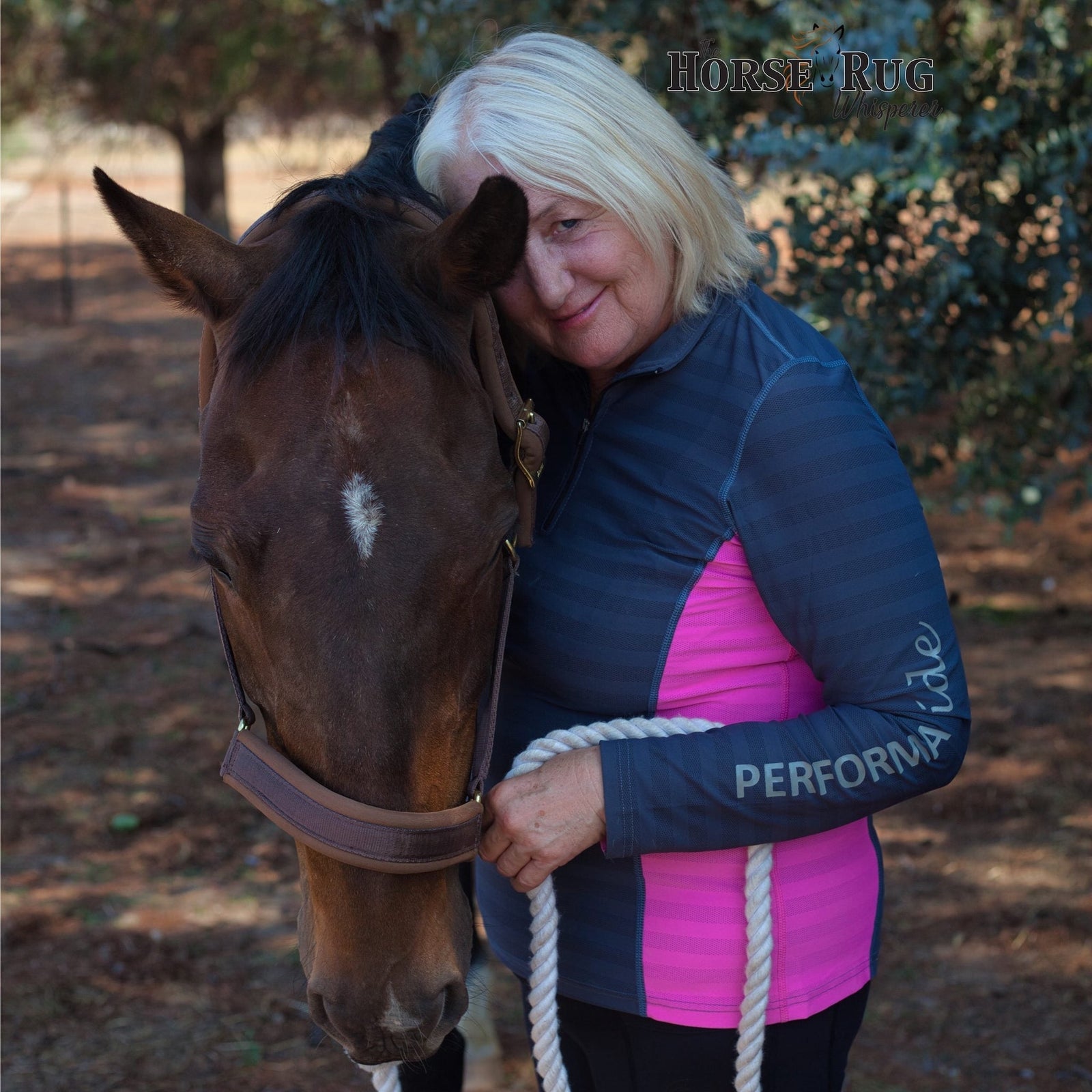 Lady wearing aqua long sleeve riding shirt with navy sides, holding horse.